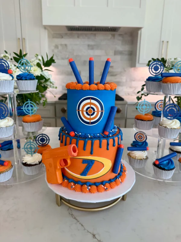 Orange and blue mini two-tier Nerf-themed cake surrounded by matching cupcakes from Little Things Kitchen